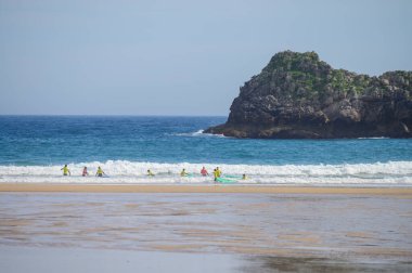 Genç sörfçüler, Celorio 'daki Playa de Palombina Las Camaras' ta, Kuzey İspanya, Asturias 'ın kumlu sahilleri, kayalıkları, gizli mağaraları, yeşil tarlaları ve dağları olan sörf tahtalimi yapıyorlar.