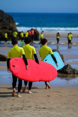 Genç sörfçüler, Celorio 'daki Playa de Palombina Las Camaras' ta, Kuzey İspanya, Asturias 'ın kumlu sahilleri, kayalıkları, gizli mağaraları, yeşil tarlaları ve dağları olan sörf tahtalimi yapıyorlar.