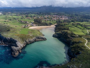 Playa de Poo 'daki hava manzarası, Llanes yakınlarındaki gelgit sırasında, Asturias, Kuzey İspanya' nın yeşil kıyıları, beyaz kumlu plajları, kayalıkları, gizli mağaraları, yeşil tarlaları ve dağları olan.