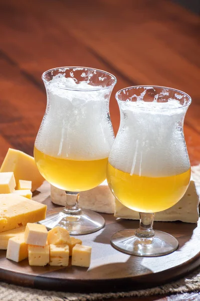 Manastırda yapılmış Belçika yapımı açık sarı bira bardakları ve çeşitli Belçika peynirleri, yiyecek ve bira eşleştirmeleri.