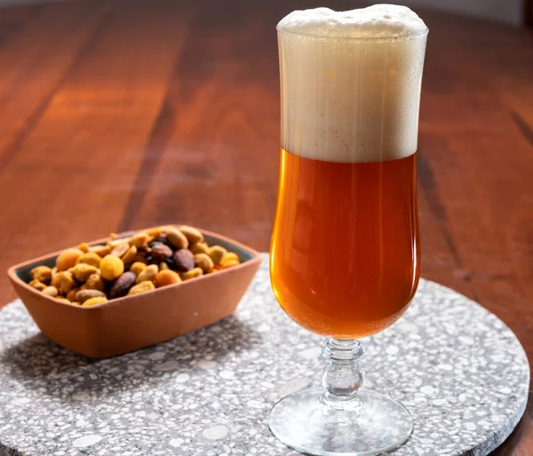 stock image Glass of Belgian light blond beer made in abbey and bowl with party mix nuts, close up