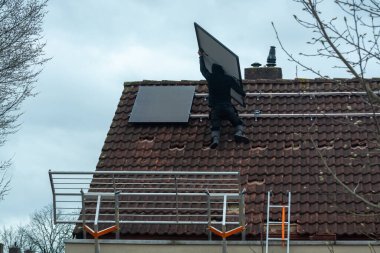 Bulutlu kış gününde evin çatısına güneş panelleri kurulması, Avrupa 'da yeşil enerji