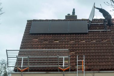 Bulutlu kış gününde evin çatısına güneş panelleri kurulması, Avrupa 'da yeşil enerji