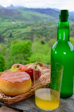 Mayalanmış elmadan yapılmış doğal Asturian şarabı ve füme peynir ve arka plandaki Picos de Europa dağlarına bakan Asturian ineği.