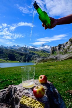 Doğal Asturya şarabı dökülüyor yeşil şişeden mayalanmış elma ve yüksek yükseklikten Covadonga Gölü ve İspanya 'nın kuzeyindeki Picos de Europa dağlarının tepeleri manzaralı