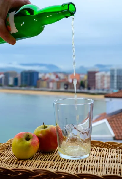 stock image Traditional natural Asturian cider made from fermented apples in wooden barrel should be poured from great height for air bubbles into the drink and view on San Lorenzo beach of Gijon