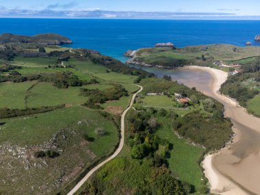 Playa de Poo 'daki hava manzarası, Llanes yakınlarındaki gelgit sırasında, Asturias, Kuzey İspanya' nın yeşil kıyıları, beyaz kumlu plajları, kayalıkları, gizli mağaraları, yeşil tarlaları ve dağları olan.