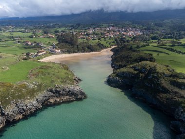 Playa de Poo 'daki hava manzarası, Llanes yakınlarındaki gelgit sırasında, Asturias, Kuzey İspanya' nın yeşil kıyıları, beyaz kumlu plajları, kayalıkları, gizli mağaraları, yeşil tarlaları ve dağları olan.