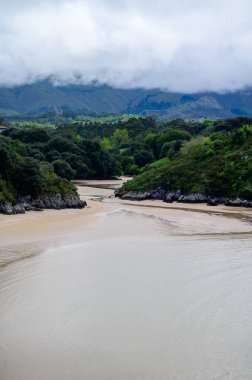 Playa de Poo 'ya bakın. Llanes yakınlarındaki gelgit sırasında, Asturias' ın yeşil kıyıları, Kuzey İspanya 'nın beyaz kumlu sahilleri, kayalıkları, gizli mağaraları, yeşil tarlaları ve dağları ile birlikte..