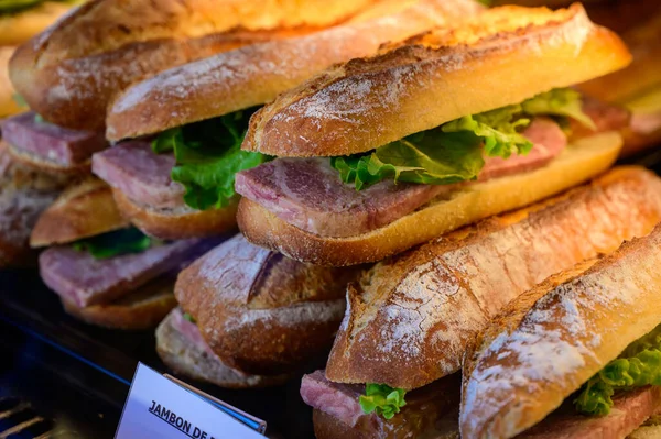 stock image Fresh made organic sandwiches with baquette buns, bacon and salad, english translation is bacon, on display in bakery in France