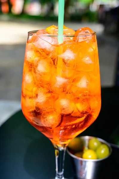 Waiter prepared the Aperol Sprits summer cocktail with Aperol, prosecco, ice cubes, tonic water and orange in wine glass, ready to drink on sunny terrace