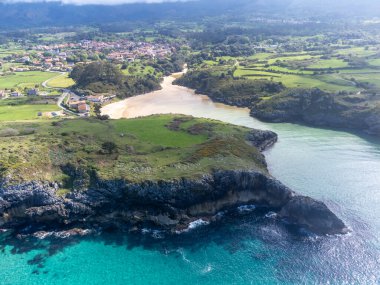 Playa de Poo 'daki hava manzarası, Llanes yakınlarındaki gelgit sırasında, Asturias, Kuzey İspanya' nın yeşil kıyıları, beyaz kumlu plajları, kayalıkları, gizli mağaraları, yeşil tarlaları ve dağları olan.
