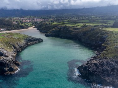Playa de Poo 'daki hava manzarası, Llanes yakınlarındaki gelgit sırasında, Asturias, Kuzey İspanya' nın yeşil kıyıları, beyaz kumlu plajları, kayalıkları, gizli mağaraları, yeşil tarlaları ve dağları olan.