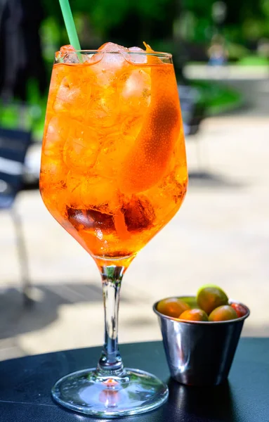 Waiter prepared the Aperol Sprits summer cocktail with Aperol, prosecco, ice cubes, tonic water and orange in wine glass, ready to drink on sunny terrace