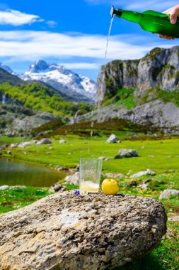 Yeşil şişeden ve yüksek miktarda mayalanmış elmadan yapılmış doğal Asturian şarabından akan Covadonga Gölü ve İspanya 'nın kuzeyindeki Picos de Europa dağlarının tepeleri manzaralı