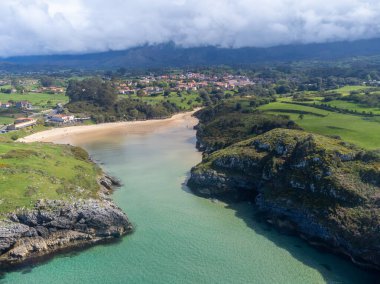 Playa de Poo 'daki hava manzarası, Llanes yakınlarındaki gelgit sırasında, Asturias, Kuzey İspanya' nın yeşil kıyıları, beyaz kumlu plajları, kayalıkları, gizli mağaraları, yeşil tarlaları ve dağları olan.