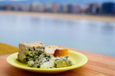 Arenas 'tan gelen mavi inek peyniriyle San Lorenzo plajı ve iGijon evleri manzaralı servis ediliyor.