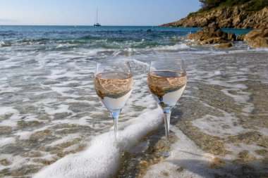 Provence 'de yaz mevsimi, güneşli bir günde Saint-Tropez yakınlarındaki kumlu sahilde iki bardak soğuk gül şarabı, Var Bölümü, Fransa.