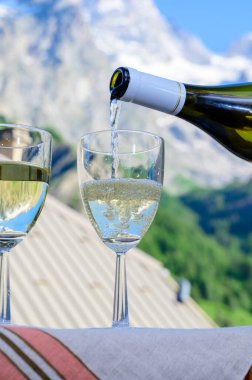 Kuru beyaz Roussette de Savoie ve Savoy bölgesinden Vin de Savoie Fransız şarabı içerken, üzerinde kar olan Hautes Alpes dağları manzaralı
