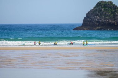 Genç sörfçüler, Celorio 'daki Playa de Palombina Las Camaras' ta, Kuzey İspanya, Asturias 'ın kumlu sahilleri, kayalıkları, gizli mağaraları, yeşil tarlaları ve dağları olan sörf tahtalimi yapıyorlar.