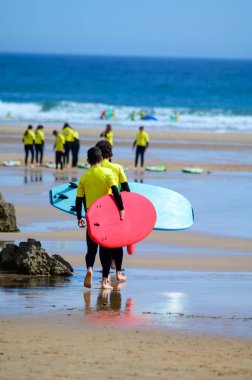Genç sörfçüler, Celorio 'daki Playa de Palombina Las Camaras' ta, Kuzey İspanya, Asturias 'ın kumlu sahilleri, kayalıkları, gizli mağaraları, yeşil tarlaları ve dağları olan sörf tahtalimi yapıyorlar.