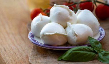 Beyaz küçük İtalyan yumuşak peyniri Mozzarella di Bufala Campana topları taze yeşil fesleğen ve kırmızı Sicilya domatesleriyle servis edilir.