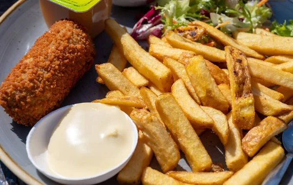 Dutch fast food, deep fried croquettes filled with ground beef meat and french fried potatoes chips served with mayonnaise, green salad, close up