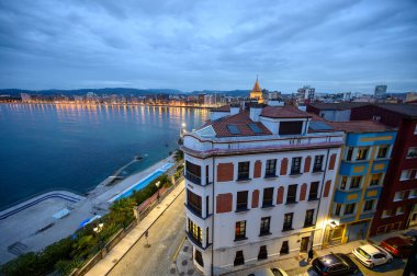 Gijon, Asturias, İspanya 'daki gezinti güvertesi, evler ve San Lorenzo plajında akşam manzarası