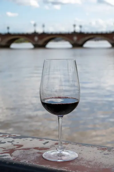 Tasting of Bordeaux blended red wine with wine city Bordeaux on background, left bank of Gironde Estuary, France. Glass of red French wine served outdoor.