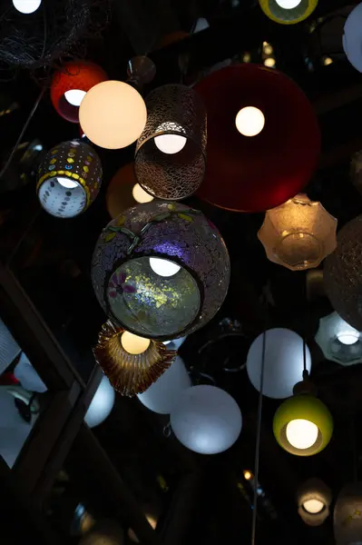 Many different ceiling lamps with lightbulbs in dark room with wall mirrors