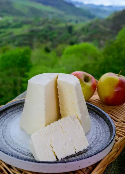 Spanish Afuega\'l pitu unpasteurised cow\'s milk cheese from Asturias served outdoor with apples and view on green slopes of Picos de Europa mountains, Spain