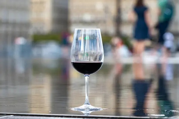 Tasting of Bordeaux blended red wine with wine city Bordeaux on background, left bank of Gironde Estuary, France. Glass of red French wine served outdoor.