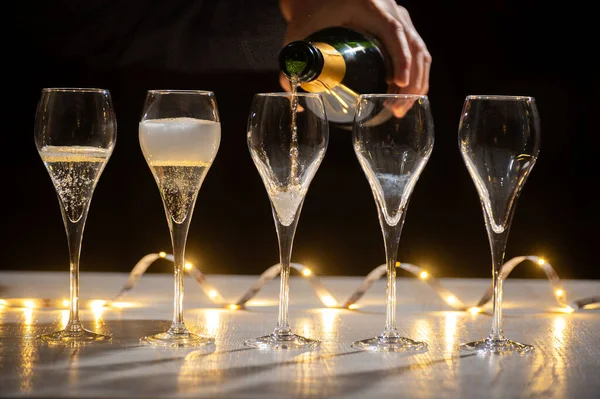 Yeni yıl partisi, koyu arka planda çelenk ışıkları olan lale bardaklarında brut şampanya, kava ya da Prosecco şarabı.