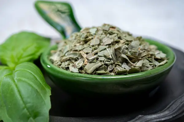 Dried crushed and whole fresh leaves of green aromatic basil plant used for cooking and medicine close up