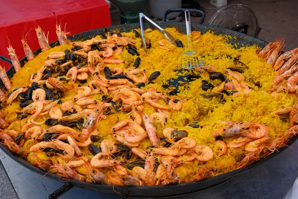 Street food in France, fresh prepared colorful paella with rice and sea food in big pan on street market ready to eat
