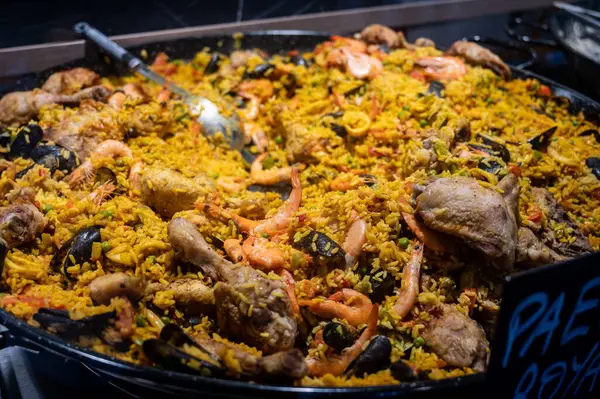 Street food in France, fresh hot prepared colorful paella with rice and sea food in big pan on street market ready to eat