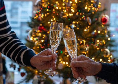 Yeni yıl ya da Noel yemeği, elinde şampanya bardakları olan iki erkek eli ya da kristal bardaklarda şarap ve arka planda Noel ağacı ve çelenk ışıkları.