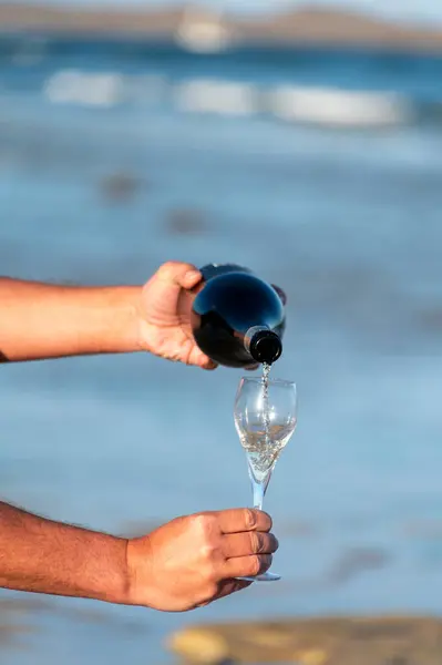 Pouring of cava or champagne sparkling wine on vacation, Dunes Corralejo sandy beach, Fuerteventura, Canary islands on sunset