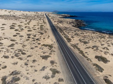 Corralejo sahili yakınlarındaki beyaz kumlu kumsallarda, siyah asfalt yolda araba sürmek Fuerteventura, Kanarya Adaları, İspanya kışın