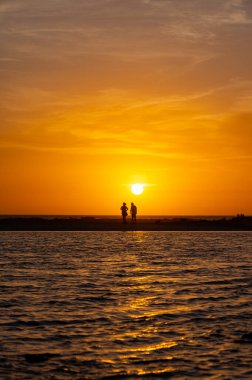 Erkek ve kadın kalıp okyanus sahilinde gün batımını izliyorlar, turuncu gökyüzü, tatildeki insanların siluetleri, Kanarya adaları.