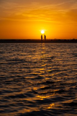 Erkek ve kadın kalıp okyanus sahilinde gün batımını izliyorlar, turuncu gökyüzü, tatildeki insanların siluetleri, Kanarya adaları.
