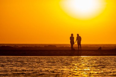 Erkek ve kadın kalıp okyanus sahilinde gün batımını izliyorlar, turuncu gökyüzü, tatildeki insanların siluetleri, Kanarya adaları.