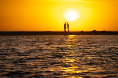 Erkek ve kadın kalıp okyanus sahilinde gün batımını izliyorlar, turuncu gökyüzü, tatildeki insanların siluetleri, Kanarya adaları.