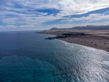 Caleta del bajo, Corralejo grandes, İspanya 'nın Kanarya Adaları, Fuerteventura' nın kuzeyindeki Corralejo turistik kasabası yakınlarında mavi sulu beyaz kumlu plajlarda oynuyor.