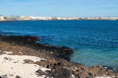 Beyaz mercanlar, siyah kayalar, mavi sular, Fuerteventura, Kanarya adaları, İspanya 'nın beyaz patlamış mısır plajı boyunca Corralejo kasabasında deniz gezintisi.