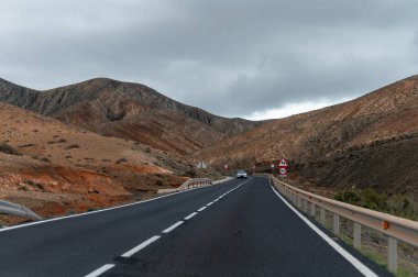 Betancuria Massif, Fuerteventura, Kanarya Adaları, İspanya 'nın renkli uzak bazal tepeleri ve dağları üzerindeki dağ asfalt yolu.