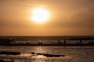Erkek ve kadın kalıp okyanus sahilinde gün batımını izliyorlar, turuncu gökyüzü, tatildeki insanların siluetleri, Kanarya adaları.