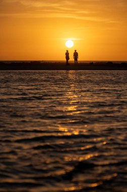 Erkek ve kadın kalıp okyanus sahilinde gün batımını izliyorlar, turuncu gökyüzü, tatildeki insanların siluetleri, Kanarya adaları.