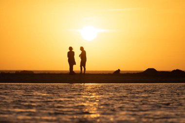 Erkek ve kadın kalıp okyanus sahilinde gün batımını izliyorlar, turuncu gökyüzü, tatildeki insanların siluetleri, Kanarya adaları.