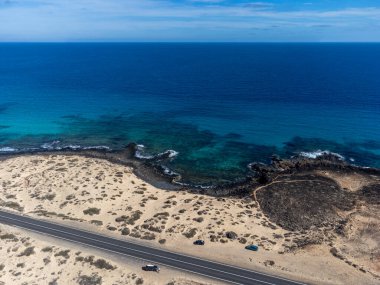 Corralejo sahili yakınlarındaki beyaz kumlu kumsallarda, siyah asfalt yolda araba sürmek Fuerteventura, Kanarya Adaları, İspanya kışın